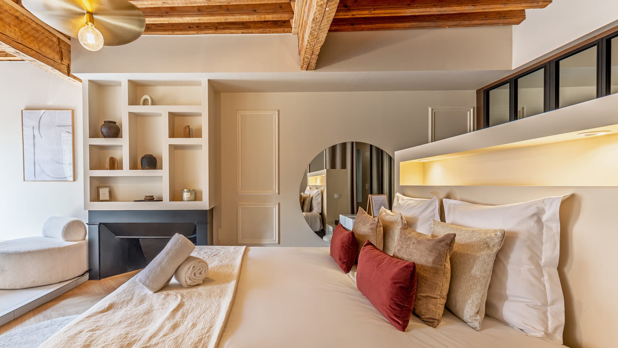 Lit king-size habillé de coussins, ambiance feutrée sous poutres apparentes